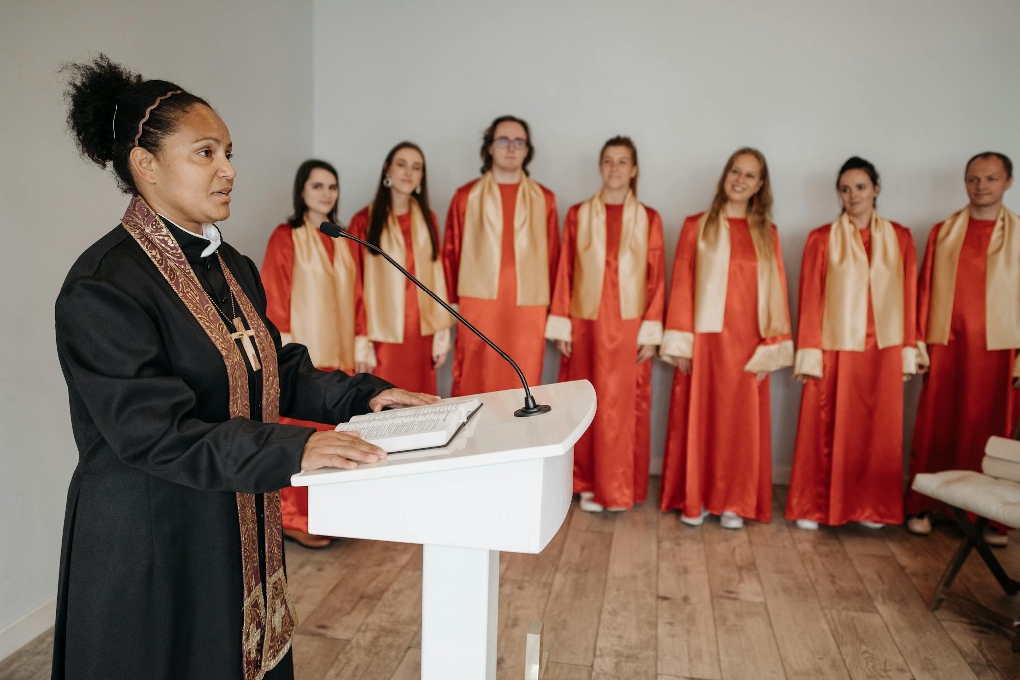 A pastor delivers a sermon at a podium with a choir standing behind.